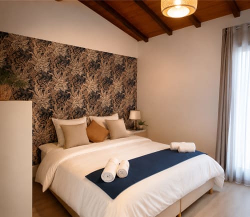Dormitorio elegante en Casa Grande de Covas con pared de acento estampada, ropa de cama color crema, camino azul oscuro, toallas enrolladas y