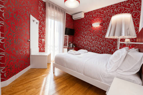 Camera luminosa al B&B Pellicano di Reggio Calabria con carta da parati rossa a fantasia, letto bianco, pavimento in legno e accesso al balcone