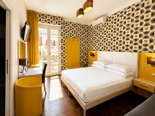 Camera moderna presso il B&B Pellicano di Reggio Calabria con accenti gialli, carta da parati a fiori, letto bianco e vista città