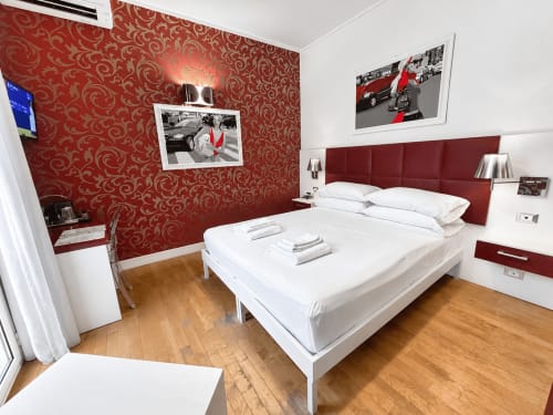 Moderna camera doppia al B&B Pellicano di Reggio Calabria con carta da parati rossa decorata, biancheria bianca e pavimenti in legno.