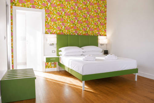 Camera da letto moderna e luminosa a B&B Pellicano con letto verde, biancheria bianca, carta da parati floreale colorata e pavimenti in legno