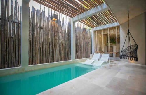 Piscina cubierta de Zen Stays con agua turquesa, tumbonas blancas, silla colgante, mamparas de madera y techo con tragaluz en Tulum.