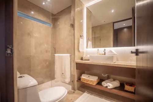 Modern bathroom at Zen Stays Tulum with glass shower, white sink, toilet, and wooden vanity storage.