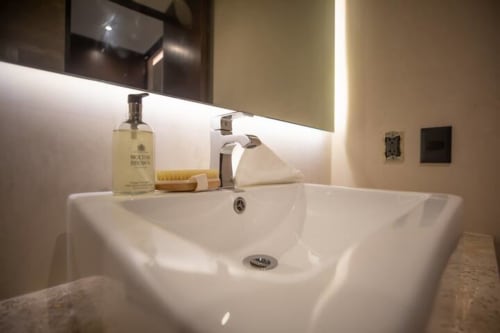 Lavamanos moderno en Zen Stays Tulum con lavabo blanco, amenidades y espejo iluminado
