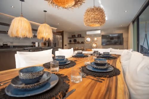Modern dining area at Zen Stays Tulum with natural fiber pendant lights, wooden table, blue place settings, and open kitchen