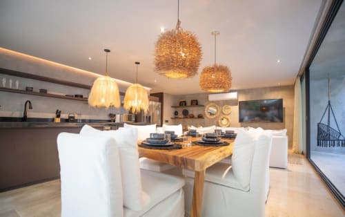 Modern Tulum hotel dining area with white chairs, wooden table, and woven pendant lights at Zen Stays