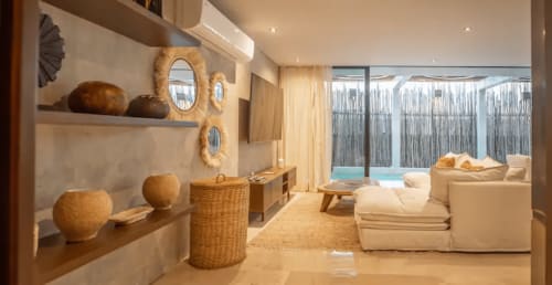 Zen Stays Tulum resort lounge with wooden furnishings, woven decor, cream seating, and pool view through glass doors