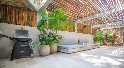 Área lounge moderna con pérgola en Zen Stays Tulum, plantas en macetas, asientos y parrilla Weber bajo listones de madera