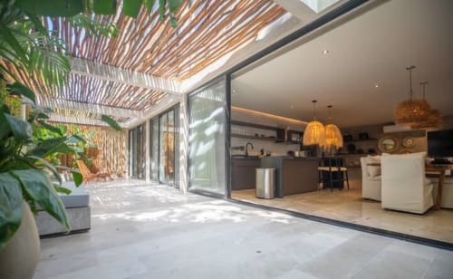 Patio moderno en Zen Stays Tulum con pérgola de madera, plantas en macetas y puertas de vidrio que abren a una cocina contemporánea