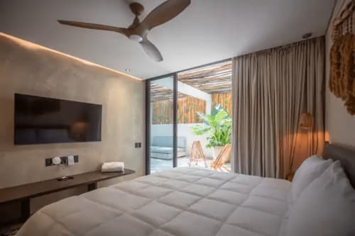 Modern bedroom at Zen Stays Tulum with white bedding, flat-screen TV, ceiling fan, and ocean-view patio access