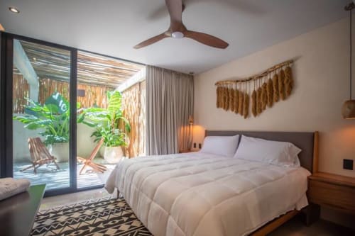 Modern bedroom at Zen Stays Tulum with king bed, ceiling fan, and outdoor garden access through glass doors