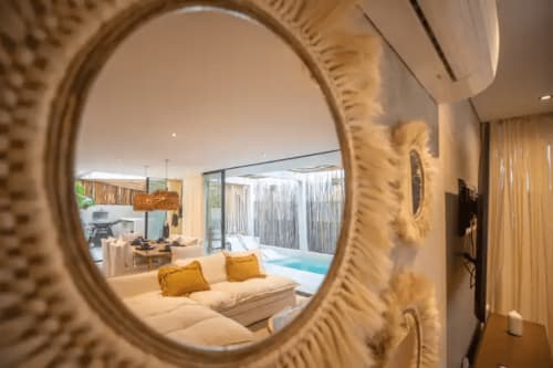 Zen Stays luxury suite in Tulum featuring cream sofa with gold pillows, ornate mirror, and pool view through modern glass