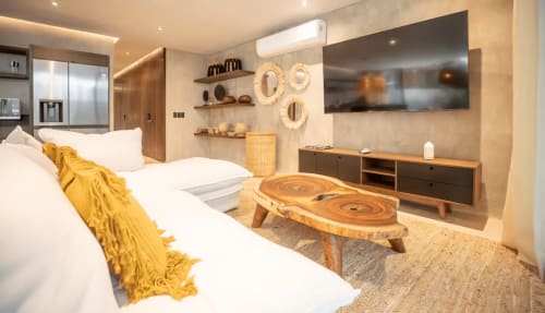 Dormitorio moderno en Zen Stays Tulum con cama blanca, muebles de madera, TV montada en pared y acentos decorativos naturales