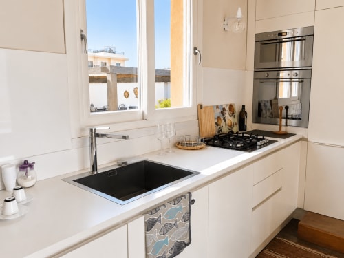 Cucina moderna con vista sul mare, fornello a gas, lavello nero e mobili bianchi nel B&B di Reggio Calabria