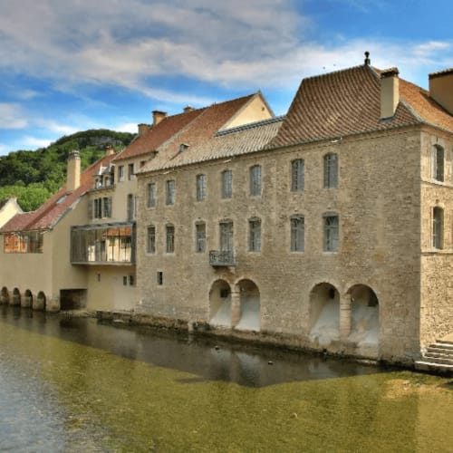 Gîte La Truite d'Or stone building with arched waterfront openings in Lods, France