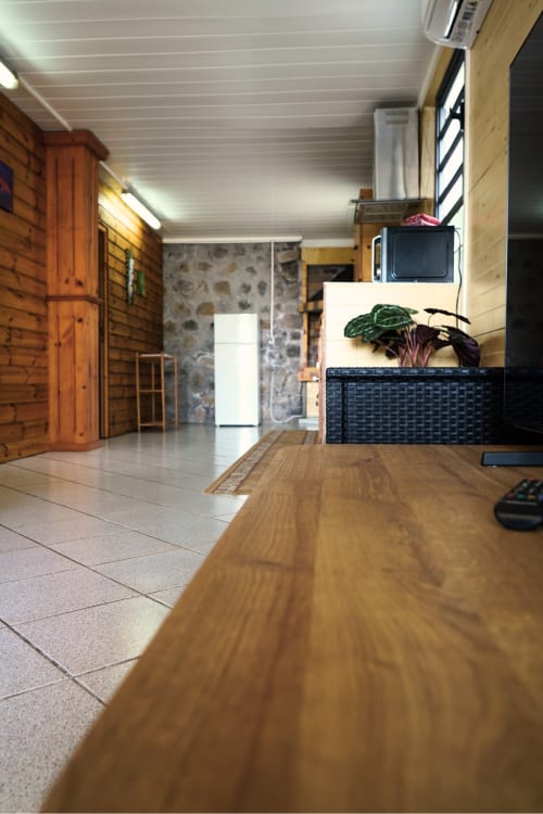 Bungalow Le Cocotier R'marine439 : séjour-salle à manger ouvert avec table en bois, murs en pierre, TV et climatisation