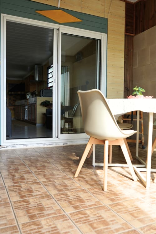 Terrasse du bungalow Le Cocotier à R'marine439 à Sainte-Rose avec chaise moderne et table à manger donnant sur l'intérieur