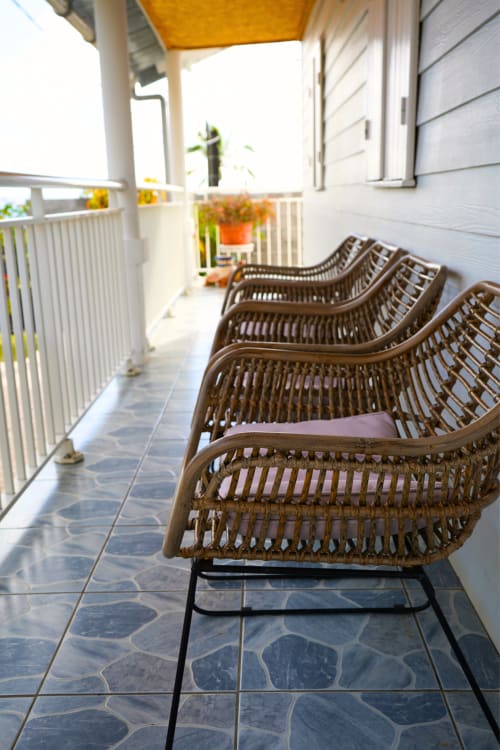 Chaises longues en rotin tressé sur terrasse carrelée du gîte R'marine439 à Sainte-Rose, parasol jaune et vue sur le jardin