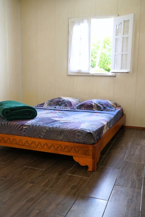 Chambre de la cabane Caz' mangoustan au R'marine439 BnB, Sainte-Rose, avec lit en bois, parure bleue, vue sur le jardin et