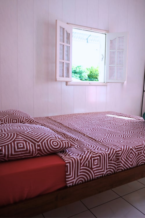 Chambre rose avec linge de lit à motifs et fenêtre ouverte sur le jardin du gîte R'marine439, Sainte-Rose