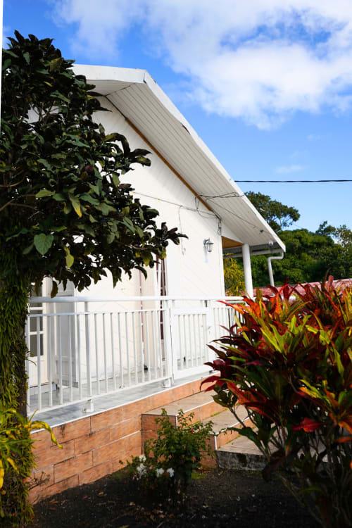 Cottage blanc avec vue sur jardin à la R'marine439 BnB à Sainte-Rose, balustrades blanches et plantes tropicales colorées