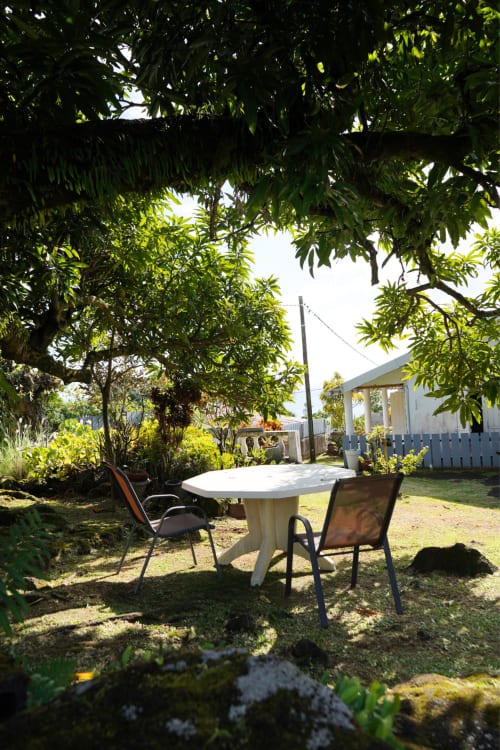 Coin détente du gîte R'marine439 à Sainte-Rose avec table blanche, chaises et luxuriante végétation tropicale