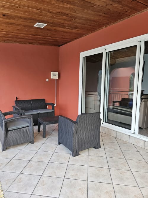 Terrasse couverte à Villa Cœur des laves à Sainte Rose avec mobilier en rotin, murs corail et vue sur mer