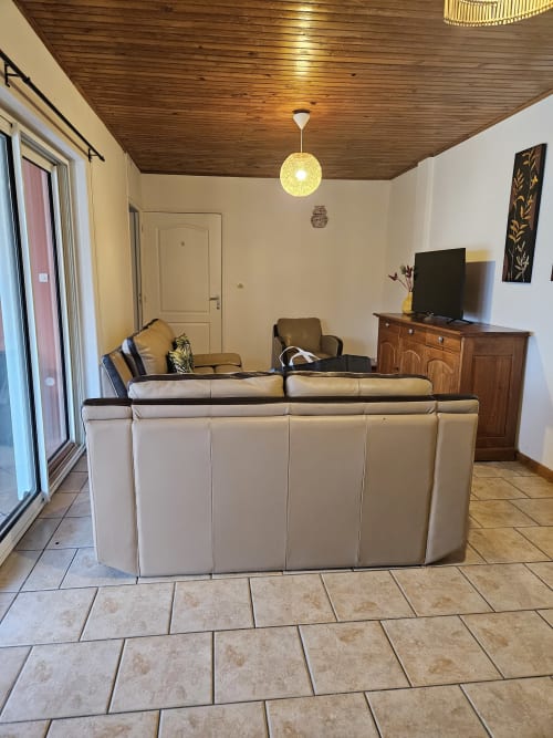 Salon spacieux de la villa R'marine439 avec canapé sectionnel beige, TV écran plat, commode en bois et balcon vue mer