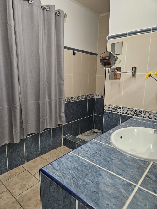 Salle de bain moderne à la Villa Cœur des laves du gîte R'marine439, Sainte Rose, avec douche carrelée bleue, lavabo blanc et rideau gris