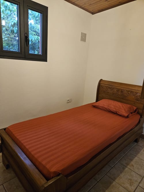 Lit en bois avec literie orange dans la chambre de la villa à R'marine439 Sainte Rose, Réunion, avec fenêtre donnant sur le jardin
