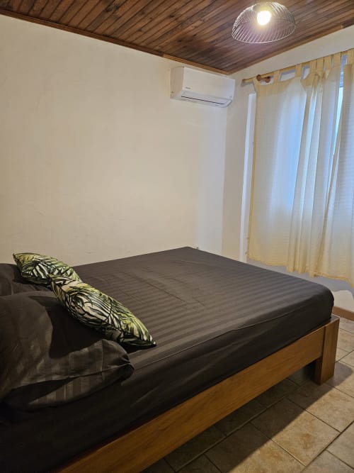 Chambre moderne avec plafond en bois, lit foncé aux coussins tropicaux, climatisation et vue mer à la villa R'marine439