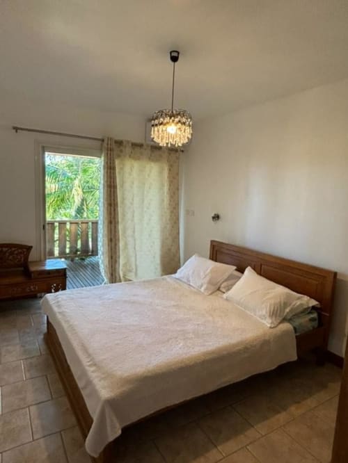 Chambre spacieuse à la Villa Cœur des laves à Sainte Rose avec lit en bois, lustre en cristal et balcon vue océan