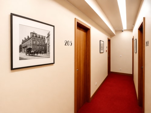 Couloir de l'Hôtel De La Poste avec portes en bois, tapis rouge et gravure architecturale encadrée à Esch-sur-Alzette