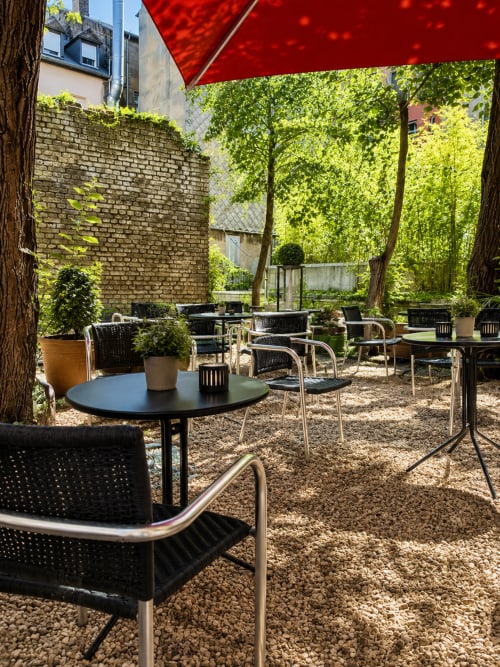Cour extérieure de l'Hôtel De La Poste à Esch-sur-Alzette avec sièges, arbres et parasol rouge