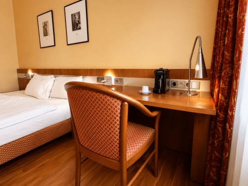 Chambre confort de l'Hôtel De La Poste avec bureau, mobilier en bois, lit aux draps blancs et éclairage chaleureux à Esch-sur-Alzette