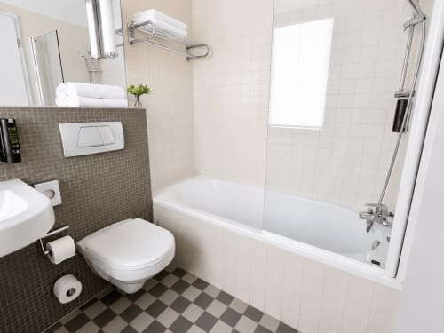 Salle de bains moderne à l'Hôtel De La Poste avec baignoire blanche, douche, toilettes et carrelage gris à Esch-sur-Alzette