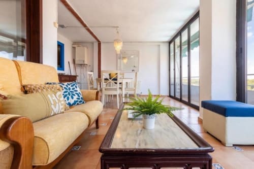 Bright Salou apartment living room with yellow sofa, marble table, fern plant, and ocean-view balcony doors