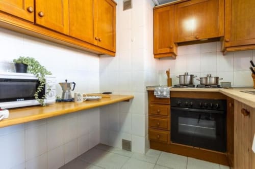 Bright kitchen in Salou apartment with wooden cabinets, white tiles, black oven, and stove