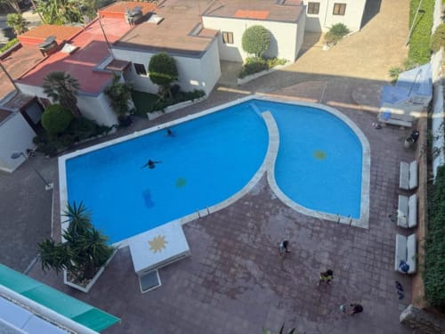 Aerial view of curved twin pools at Rentalaya apartment complex in Salou with surrounding buildings and paved deck