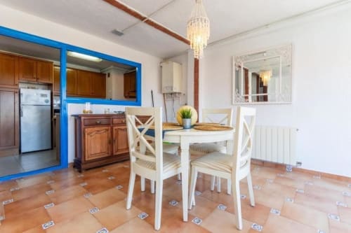 Modern kitchen-dining area in Salou apartment with white table, blue-framed kitchen, terracotta tile floors, and decorative