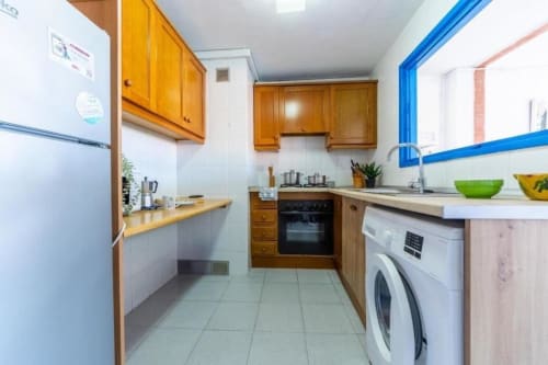 Modern kitchen in 2-bedroom Salou apartment with wooden cabinets, stainless steel appliances, and blue accent trim