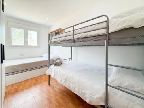 Modern bedroom with metal bunk bed, white bedding, wooden floor, window with garden view at Rentalaya villa in Reus