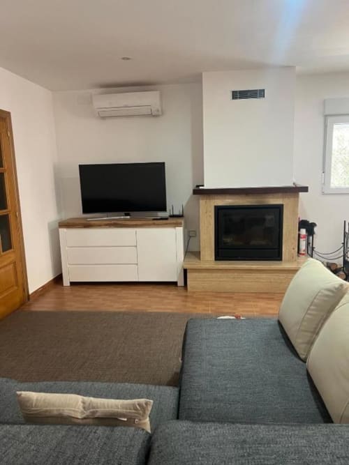 Modern living room with gray sofa, fireplace, flat-screen TV, and wooden furnishings in Rentalaya villa, Reus