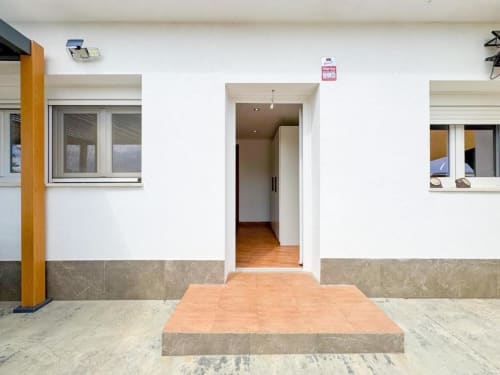 Modern villa entrance in Reus with white walls, terracotta tile flooring, and garden views at Rentalaya property