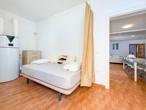 Modern villa bedroom in Reus with wooden floor, bed with canopy curtain, and adjoining living area