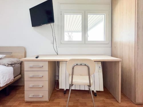 Modern villa bedroom workspace in Reus with wooden desk, chair, TV, bed, and garden view windows