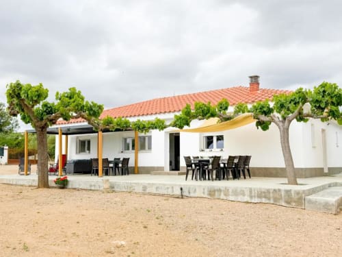 Modern villa in Reus with terracotta roof, white walls, garden views, outdoor dining area, and mature trees on sandy grounds