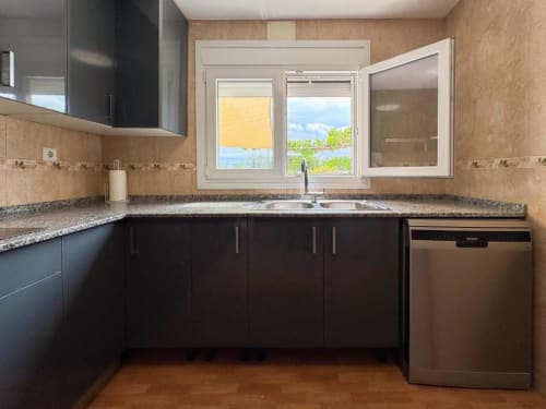 Modern kitchen with dark cabinets, granite countertop, stainless appliances, and window view in Reus villa