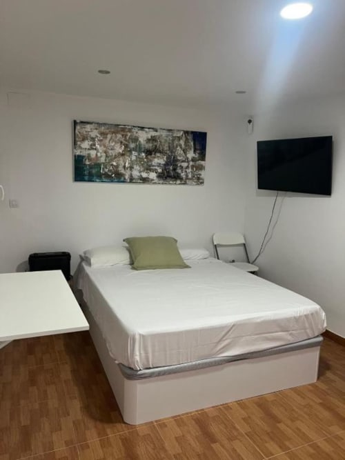Modern villa bedroom at Rentalaya in Reus with queen bed, green pillow, flat-screen TV, and abstract wall art