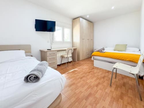 Bright villa bedroom in Reus with two beds, wooden wardrobe, desk, TV, and hardwood floors
